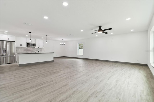 unfurnished living room featuring sink, ceiling fan with notable chandelier, and light wood-type flooring