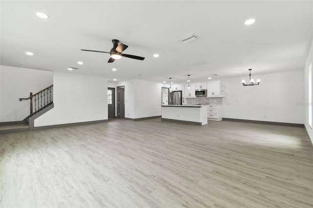 unfurnished living room featuring ceiling fan with notable chandelier and light wood-type flooring