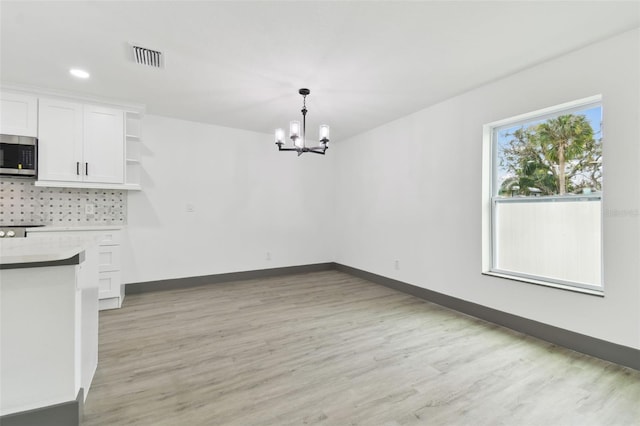 unfurnished dining area featuring an inviting chandelier and light hardwood / wood-style floors