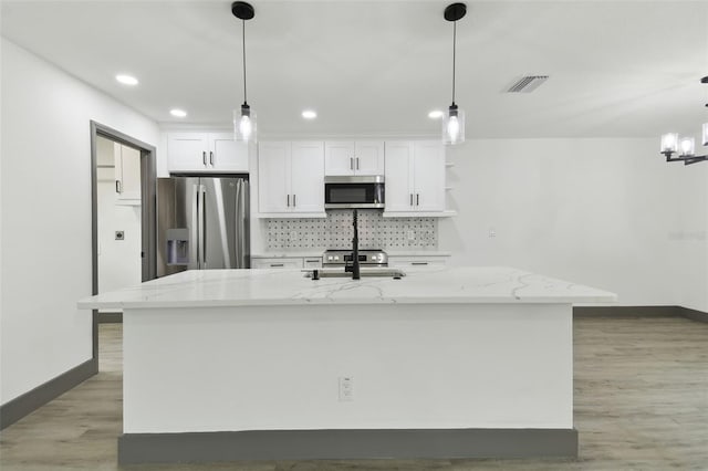 kitchen with white cabinetry, a center island with sink, appliances with stainless steel finishes, pendant lighting, and light stone countertops