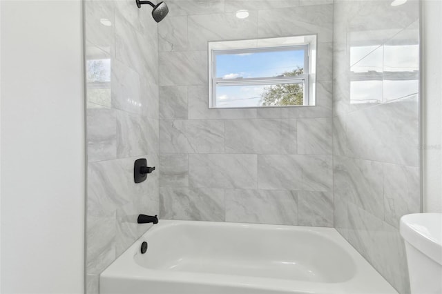 bathroom featuring toilet and tiled shower / bath