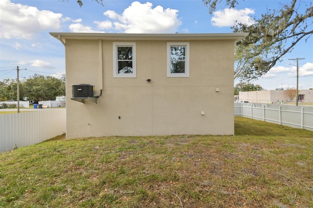 rear view of property with central AC unit and a lawn