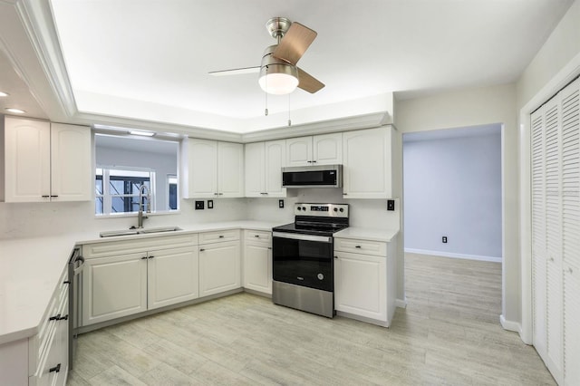 kitchen with a raised ceiling, sink, light wood-type flooring, appliances with stainless steel finishes, and white cabinetry