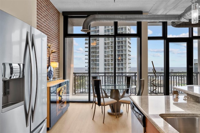 interior space featuring expansive windows, a water view, appliances with stainless steel finishes, light hardwood / wood-style floors, and light stone counters