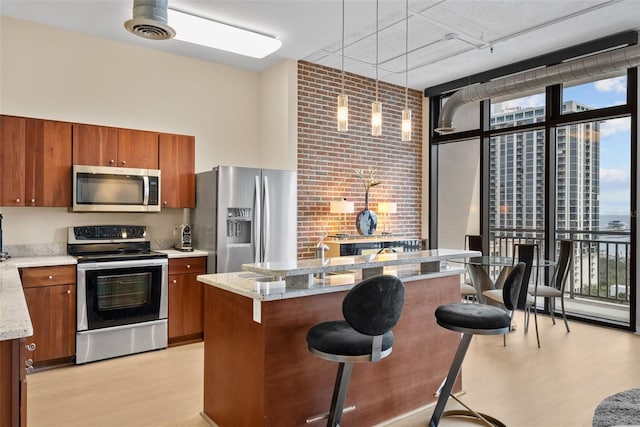 kitchen featuring appliances with stainless steel finishes, a kitchen breakfast bar, a wall of windows, a center island, and hanging light fixtures