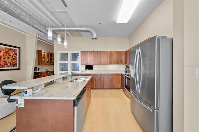 kitchen with light wood-type flooring, stainless steel appliances, a kitchen island with sink, sink, and decorative light fixtures