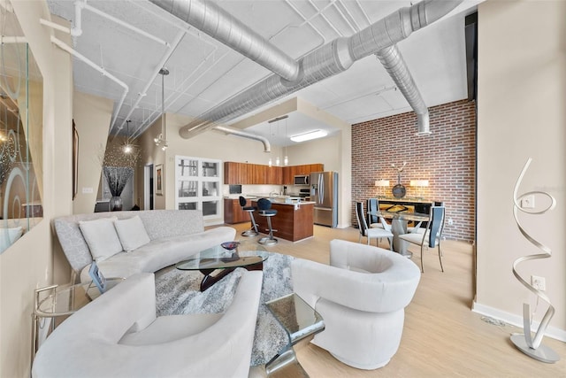 living room with a high ceiling, light hardwood / wood-style flooring, and brick wall