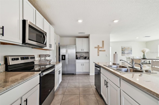 kitchen featuring sink, light tile patterned floors, appliances with stainless steel finishes, white cabinetry, and a textured ceiling