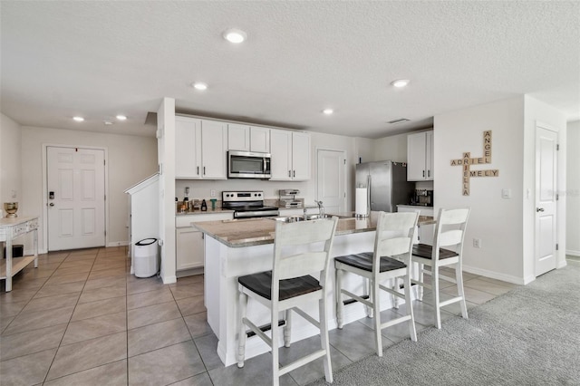 kitchen featuring a breakfast bar, white cabinetry, light tile patterned floors, stainless steel appliances, and a center island with sink