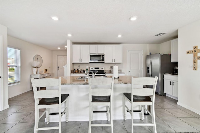 kitchen featuring white cabinetry, appliances with stainless steel finishes, an island with sink, and light stone counters