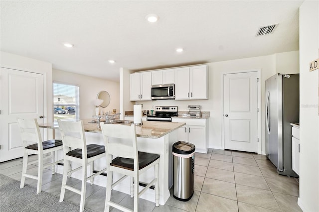 kitchen with a breakfast bar area, appliances with stainless steel finishes, light stone countertops, white cabinets, and a center island with sink