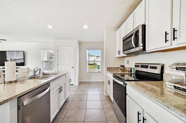 kitchen with stainless steel appliances, white cabinetry, sink, and light stone counters