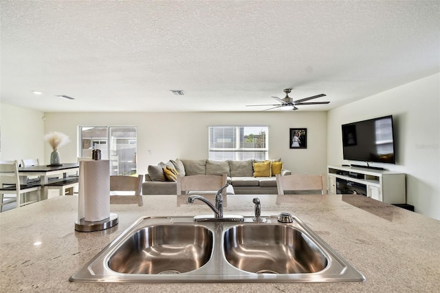 kitchen with sink, light stone countertops, a textured ceiling, and ceiling fan