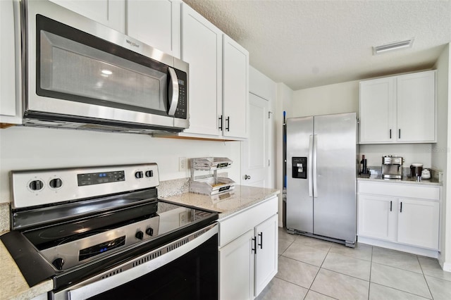 kitchen with light tile patterned floors, stainless steel appliances, light stone countertops, a textured ceiling, and white cabinets