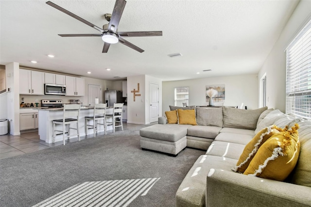 living room with ceiling fan, carpet floors, and a textured ceiling