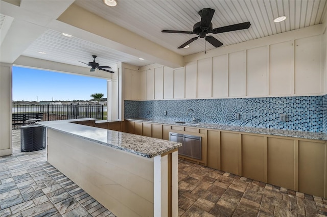 kitchen with sink, tasteful backsplash, kitchen peninsula, ceiling fan, and light stone countertops