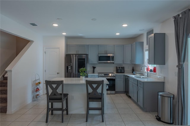 kitchen with light tile patterned flooring, sink, a kitchen island, a kitchen bar, and stainless steel appliances