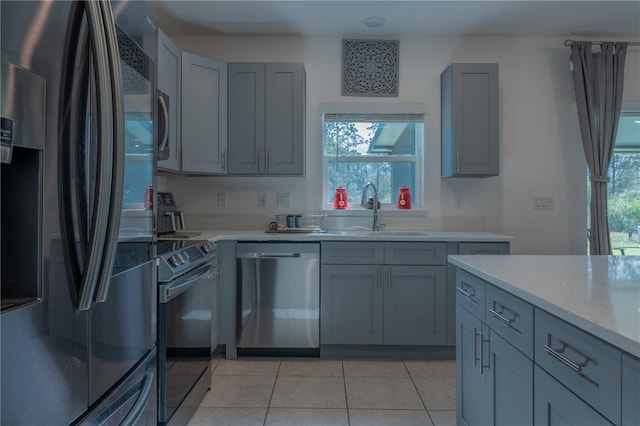 kitchen with sink, gray cabinets, appliances with stainless steel finishes, light tile patterned flooring, and light stone counters