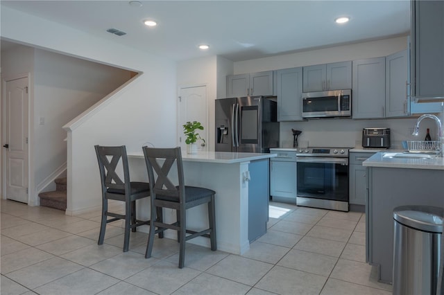 kitchen with a breakfast bar, a center island, sink, light tile patterned floors, and appliances with stainless steel finishes