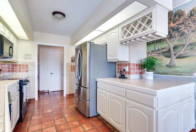 kitchen featuring tile countertops, tile walls, stainless steel fridge, white cabinets, and electric stove