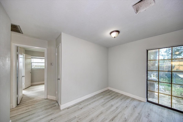 empty room with a textured ceiling and light hardwood / wood-style floors