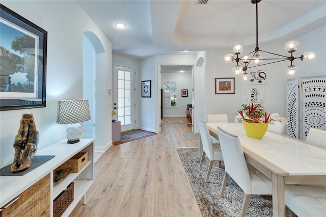 dining space featuring light hardwood / wood-style floors, a raised ceiling, and a chandelier