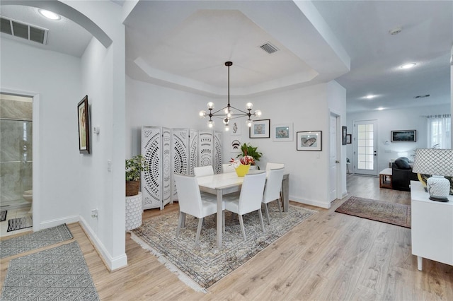 dining space with a notable chandelier, a raised ceiling, and light hardwood / wood-style floors