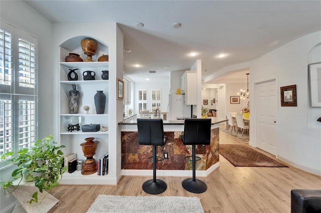 kitchen featuring decorative light fixtures, light hardwood / wood-style floors, white cabinets, and a breakfast bar