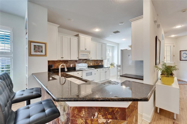 kitchen featuring white appliances, kitchen peninsula, tasteful backsplash, white cabinets, and a kitchen breakfast bar