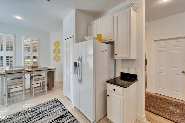 kitchen featuring a textured ceiling, white fridge with ice dispenser, light tile patterned floors, and white cabinetry