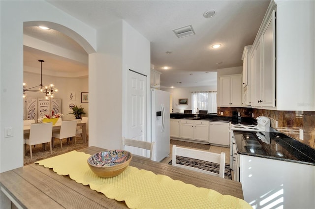 kitchen with white appliances, pendant lighting, decorative backsplash, white cabinetry, and an inviting chandelier