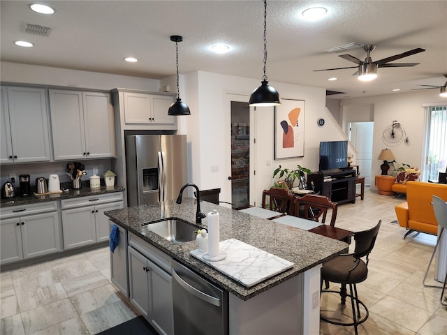 kitchen featuring pendant lighting, sink, appliances with stainless steel finishes, an island with sink, and dark stone counters