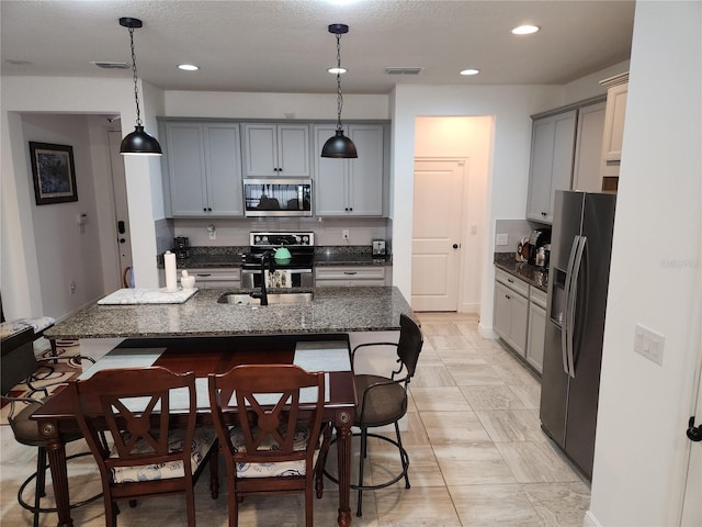 kitchen with gray cabinets, stainless steel appliances, decorative light fixtures, dark stone counters, and a breakfast bar