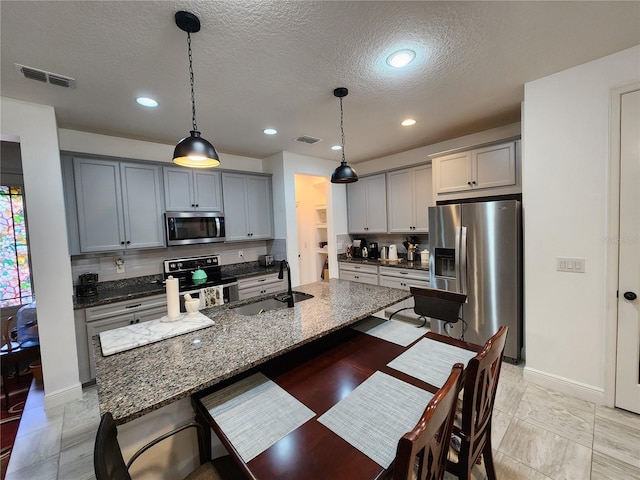 kitchen featuring decorative light fixtures, dark stone countertops, sink, appliances with stainless steel finishes, and gray cabinetry