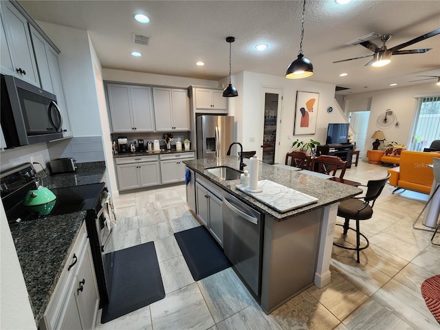 kitchen with appliances with stainless steel finishes, decorative light fixtures, sink, backsplash, and a center island with sink