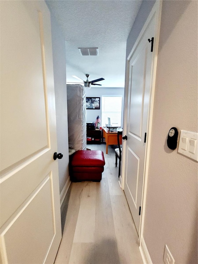 corridor with a textured ceiling and light hardwood / wood-style floors