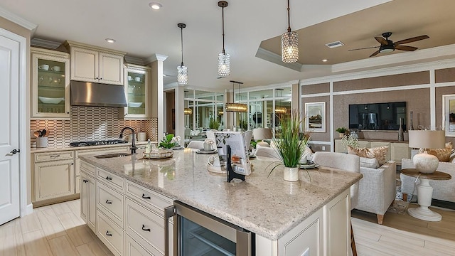 kitchen featuring hanging light fixtures, crown molding, a kitchen island with sink, and wine cooler