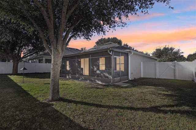 property exterior at dusk featuring a sunroom and a yard