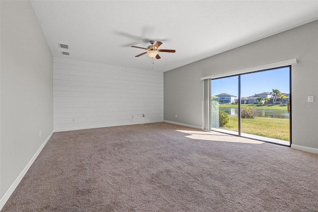 unfurnished room featuring a textured ceiling, ceiling fan, a water view, carpet floors, and wood walls