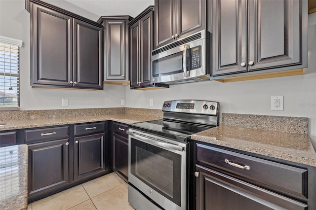 kitchen with light stone countertops, dark brown cabinets, light tile patterned flooring, and appliances with stainless steel finishes