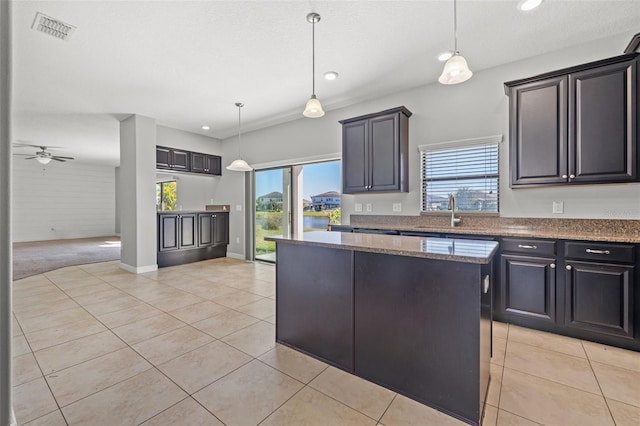 kitchen with ceiling fan, a center island, sink, hanging light fixtures, and dark stone countertops