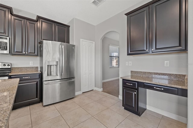 kitchen with dark brown cabinets, light tile patterned flooring, light stone counters, and appliances with stainless steel finishes