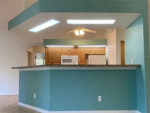 kitchen with ceiling fan, kitchen peninsula, lofted ceiling, white appliances, and light tile patterned floors