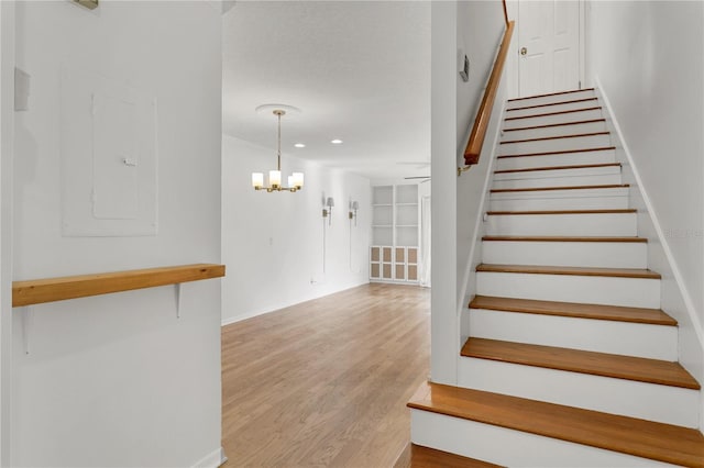 staircase featuring hardwood / wood-style floors, electric panel, and a chandelier