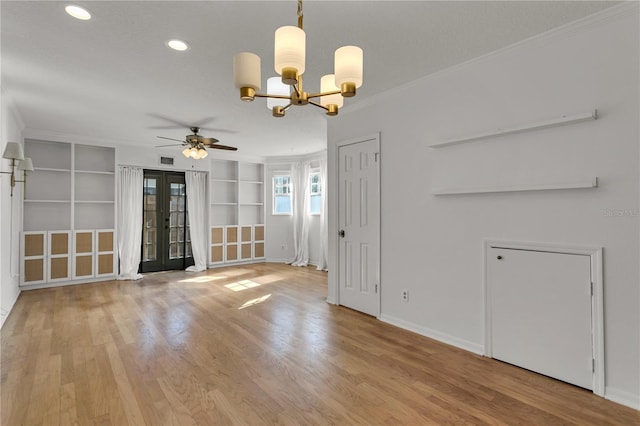 spare room featuring french doors, light wood-type flooring, ornamental molding, built in features, and ceiling fan with notable chandelier