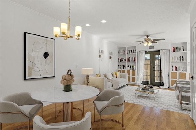 living room featuring built in features, ornamental molding, light hardwood / wood-style floors, ceiling fan with notable chandelier, and french doors