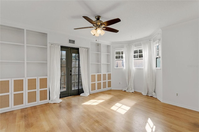 unfurnished room featuring built in features, ceiling fan, crown molding, light wood-type flooring, and french doors