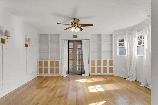 spare room with built in shelves, french doors, ornamental molding, ceiling fan, and light hardwood / wood-style floors