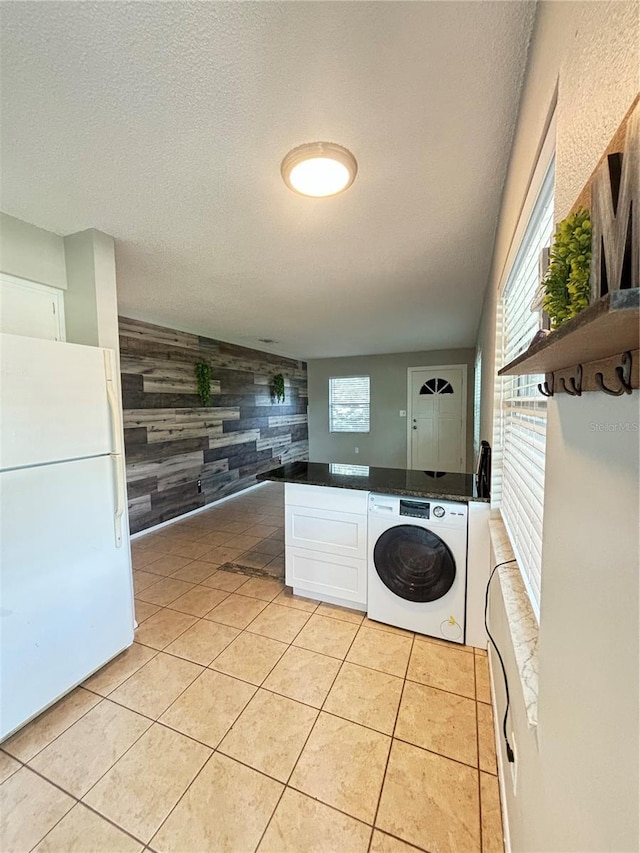 laundry area featuring a textured ceiling, washer / dryer, cabinets, wood walls, and light tile patterned floors