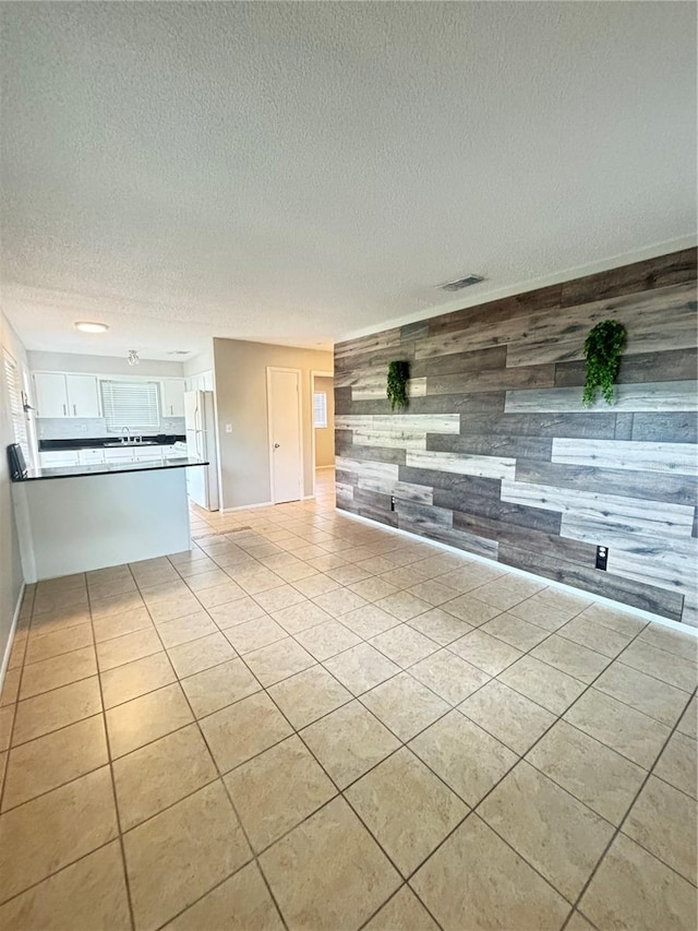 unfurnished living room featuring a textured ceiling, light tile patterned floors, and wooden walls